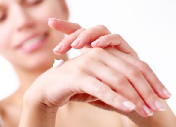 Smiling young woman applies cream on her hands on a white background