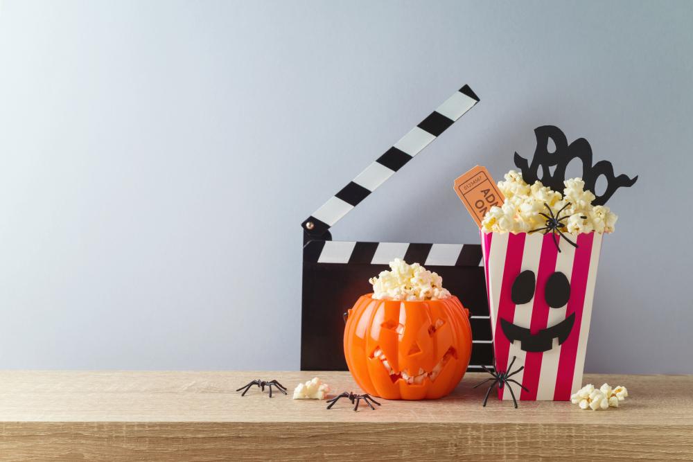 Horror movie night and halloween party concept with jack o lantern pumpkin, popcorn and movie clapperboard on wooden table