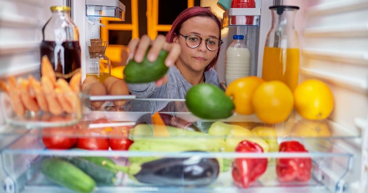 A woman placing avocados int he refrigerator