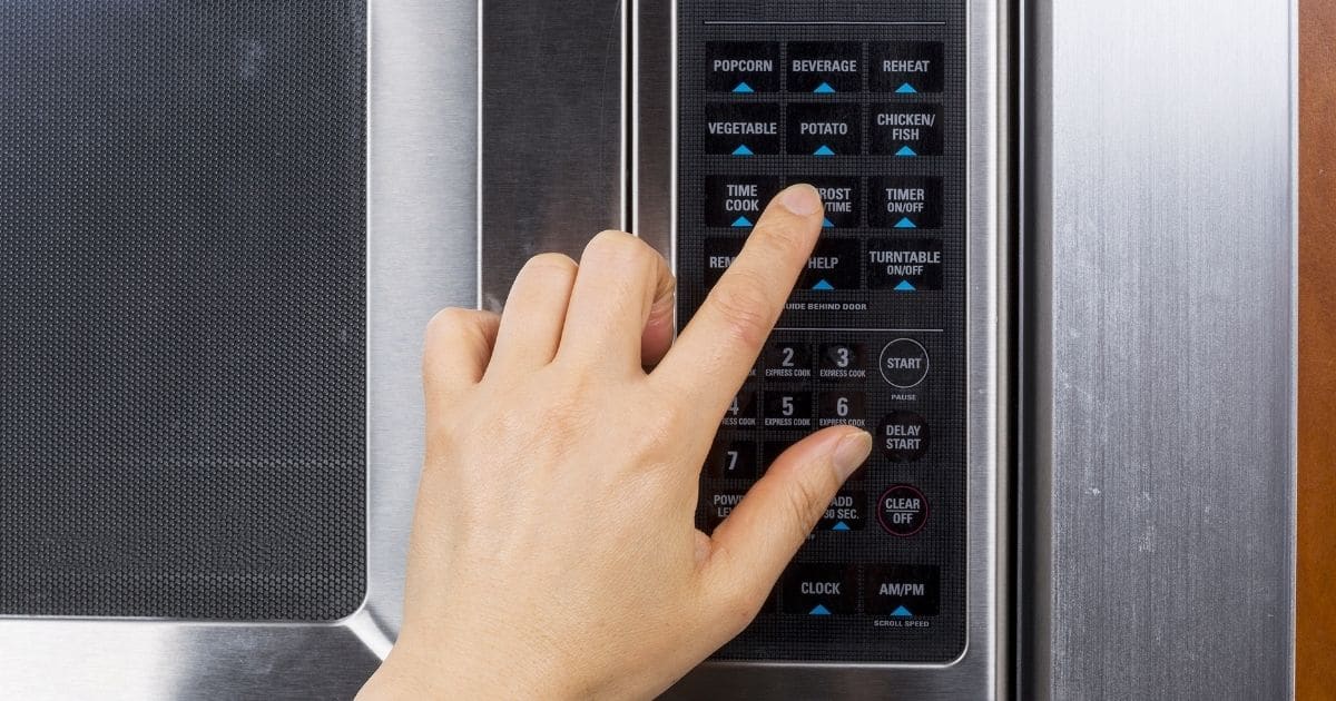 A hand using the defrost function in a microwave