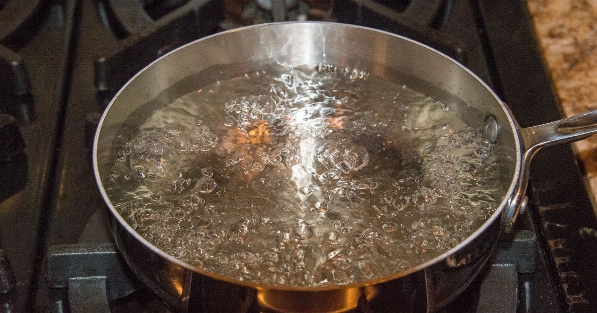 A deep pan on a gas stove with boiling water